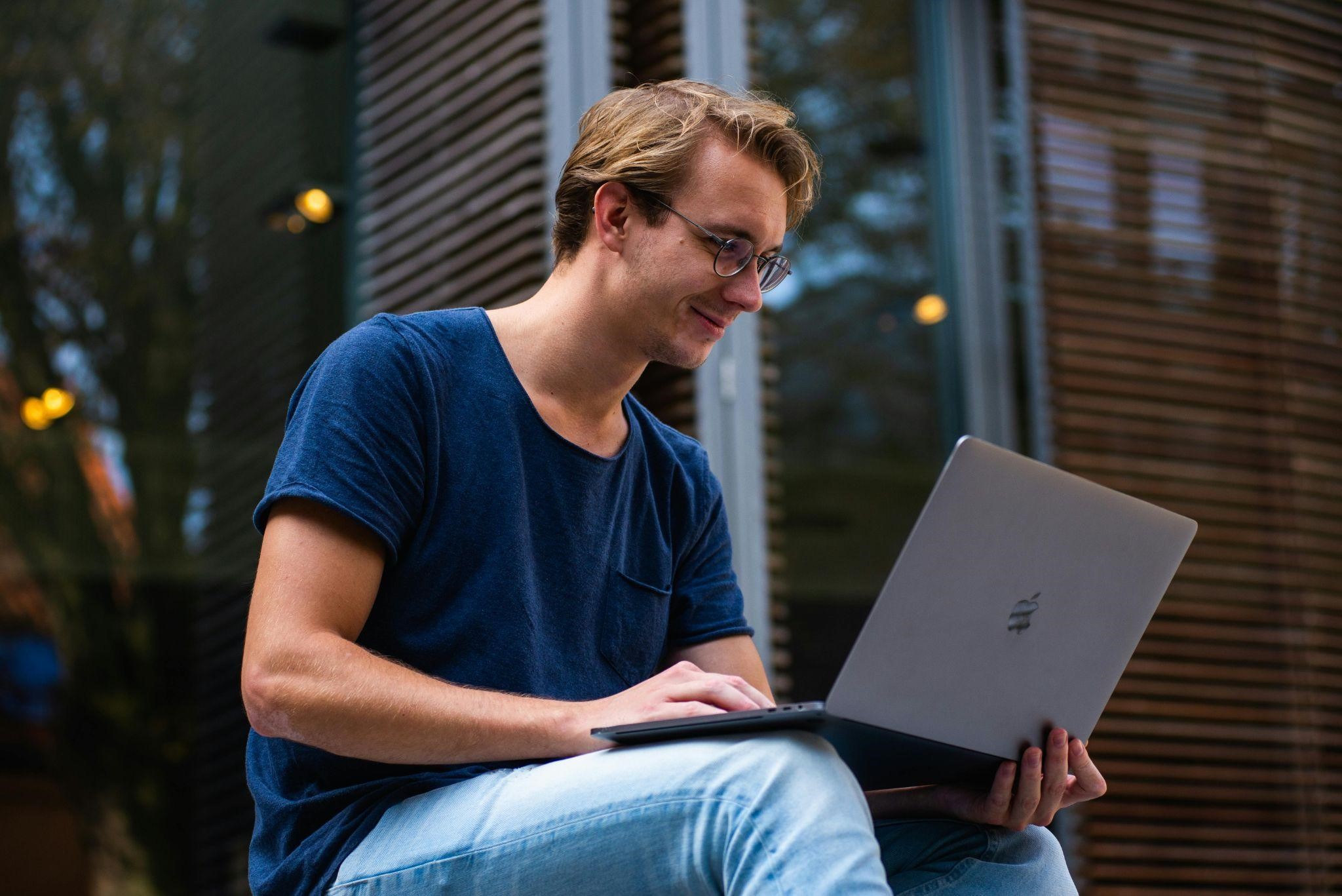 A guy sitting outdoors and using the laptop happily.